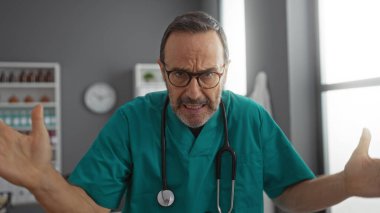 Tıbbi önlüklü orta yaşlı İspanyol bir adam hastane odasında steteskopla evde hayal kırıklığı yaşıyor..