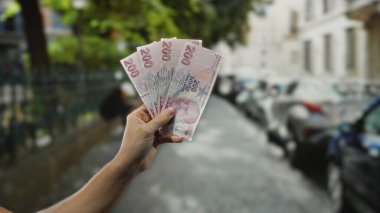 Yoğun bir şehir caddesinde elinde Türk lirası banknotları tutan, şehir ortamında para gösteren, finansal kavramları ve şehir yaşamını ön plana çıkaran bir adam..