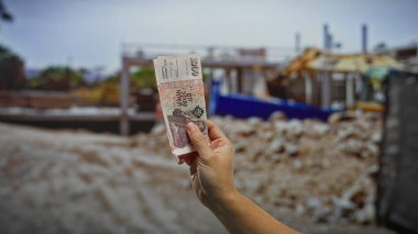 İnşaat alanı sokağında el ele tutuşan İzlanda Krona banknotları, şehirde açık havada bir adamın kentsel mali yatırımları ve döviz takasını sembolize ediyor..