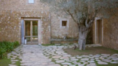 Taş ev ve ağaçlarla dolu bir Akdeniz bahçesinin bulanık görüntüsü. Bokeh etkisine sahip sakin ve kırsal bir ortam yaratıyor..