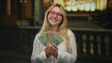 Elinde para ve arka planda renkli camlarla kilisenin içinde gülümseyen Romen banknotları tutan kadın ruhsal zenginliği artırıyor..