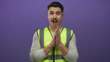 Yansıtıcı yelek giyen genç adam, izole edilmiş mor duvara karşı kamu hizmeti projesinde gönüllü olarak duruyor.