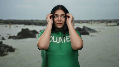 Yeşil gömlekli, deniz kenarında gönüllü olarak çalışan genç bir kadın, açık deniz çevresi ve deniz altyapısından hoşlanıyor. Toplumun katılımını ve doğa korumasını teşvik ediyor..