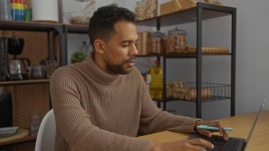 Arka planda raflar olan bir ofiste çalışan genç adam profesyonel bir atmosfer sergiliyor ve dizüstü bilgisayar kullanırken davranışlarına odaklanıyor..