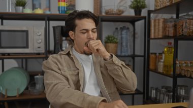 Ofis dinlenme odasında esneyen genç bir adam mikrodalga fırın ve rafları bulaşık ve mutfak malzemeleriyle dolu bir kahve makinesi..