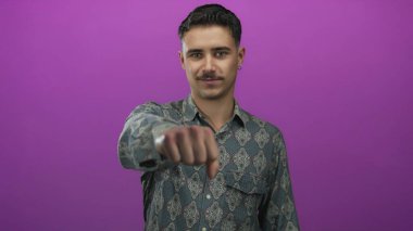 İzole edilmiş mor arka plan önünde yumruğuyla el kol hareketi yapan, kararlılık ve odaklanma gösteren, kendinden emin ve iddialı bir tavrı vurgulayan genç adam..