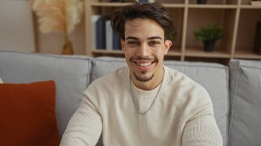 Modern apartman dairesinde gülümseyen İspanyol genç adam rahat bir yaşam tarzı ve iç mimarisi olan sıcaklığı sergiliyor..