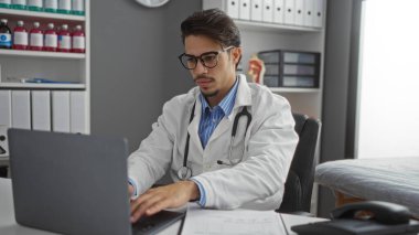 Klinikteki yakışıklı İspanyol erkek doktor laptopta çalışıyor. Konsantrasyon ve profesyonellik gösteriyor.