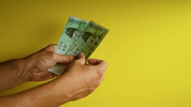 Kore 'de finans ve döviz kuru kavramını vurgulayarak, Koreli bir adamın el ele tutuşması sarı arka plana karşı banknotlar kazandı..