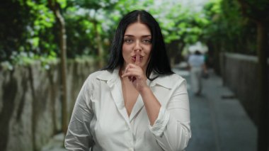 Bir kadın şehir caddesinde dışarıda dikilirken sessiz hareketler yapıyor, sakin ve huzurlu bir atmosferi somutlaştırıyor gün ışığında kentsel çevrede..