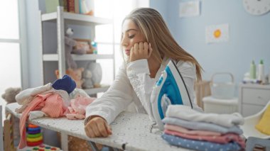 Kadın çamaşırlarını parlak çamaşır odasında ütülüyor. Düşünceli bir ifade takınıyor. Evin içinde ve güzelce katlanmış çamaşırların arasında..