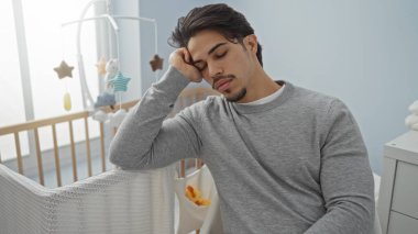 Sıcak bir yatak odasında uyuyan genç İspanyol bir adam. Bebek beşiğinin yanında. Huzurlu ve yakışıklı..