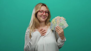 Gözlüklü genç bir kadın, elinde yeşil bir duvara karşı Romanya lei banknotları tutuyordu. Güven ve zenginlik yayıyordu. Finansal veya başarı kavramları için parlak bir arkaplanda izole edilmişti..