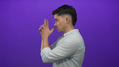 İzole edilmiş mor bir arka plan duvarına karşı parmakları silah gibi poz veren genç İspanyol adam, oyunculuk ve hayal gücünü ifade ediyor..