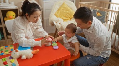 Anne ve baba, evlerinde mutlu vakit geçirirken, oyuncaklarla ve beşiğiyle çevrili rahat bir yatak odasında bebekleriyle oynuyorlar.