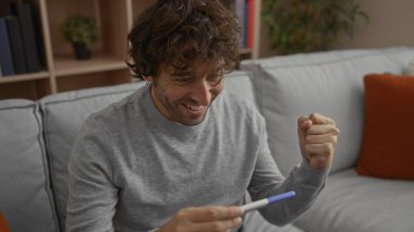 Genç adam gülümsüyor ve kucağında bir hamilelik testi tutuyor..