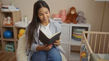 Bebek beşiği oyuncaklarla çevrili, rahat yatak odasında kitap okuyan ve huzurlu bir ortam çizen kadın..