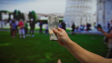 Arka planda halk ve şehir manzarası olan Pisa 'nın eğimli kulesinin önünde el ele tutuşan Endonezya rupiası..