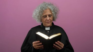 Gri saçlı kadın rahip pembe arka planda İncil okuyor..