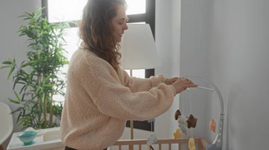 Kadın bebek arabasını rahat yatak odasında, pencerenin iç dekorunu aydınlatan doğal ışık filtresiyle ayarlıyor..