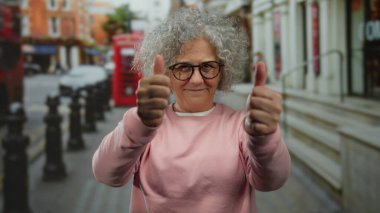 Pembe kazaklı, gri saçlı bir kadın, sembolik kırmızı telefon kulübeleriyle şehir merkezinde neşeli bir anı yakalıyor..