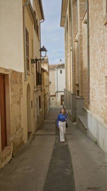 Mallorca 'nın eski kasabasında, temiz gökyüzünün altında büyüleyici dar bir sokakta yürüyen bir kadın, Akdeniz mimarisinin ve canlı kültürel atmosferinin özünü yakalıyor..