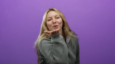 Gülümseyen bir kadın mor arka planda süveter giyiyor.