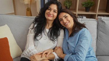 İki olgun kadın sıcak bir kanepede oturup sıcak dekore edilmiş bir oturma odasında aile sevgisini ve arkadaşlığını sembolize ederek davetkar ve samimi bir ev atmosferi sergiliyorlar..