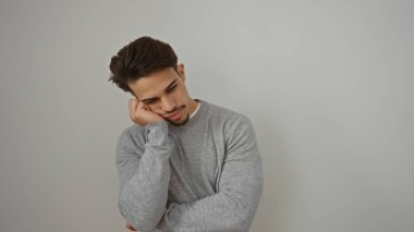 Gündelik giysiler içindeki genç adam, beyaz bir arka plana karşı düşünceli bir şekilde poz veriyor. Düşünce ve tarz sahibi, yakışıklı ve çekici bir tavır sergiliyor..