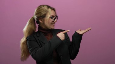 Gözlüklü bir kadın, pembe bir arka plana karşı gülümsüyor, kendine güvenen ve profesyonel bir tavır sergiliyor..