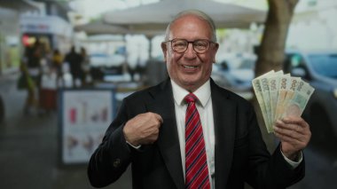 Czech Koruna banknotlarını elinde tutan kıdemli bir adam hareketli bir açık hava restoranının terasında iş ortamında neşe ifade ediyor..