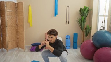 İspanyol adam iyi donanımlı bir spor salonunda çeşitli spor ekipmanlarıyla egzersiz yapıyor, iç spor merkezinde odaklanmış bir egzersiz rutini sergiliyor..