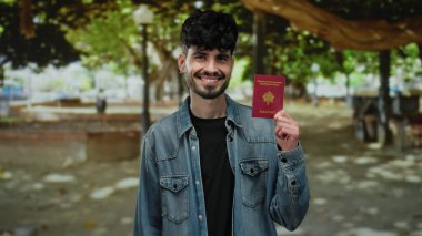 Fransız pasaportlu bir adam, yeşil ağaçlarla çevrili sakin şehir ortamının ortasında güvenli bir şekilde gülümsüyor, patikada yumuşak gölgeler bırakıyor..