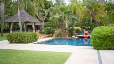 Havuzu ve yemyeşil yemyeşil verimli havuzu olan lüks bir tropikal tatil köyünün bulanık manzarası sakin bir açık hava ortamı yaratıyor..