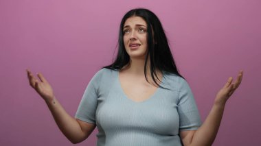 Kadın, izole edilmiş pembe arka plan, açık mavi gömlek, artı beden, kıvrımlı, uzun siyah saç, kapalı bir ifade tarzıyla hayal kırıklığını ifade ediyor..