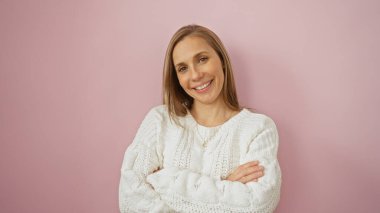 Pembe arka planda rahat bir süveter giymiş, kollarını kavuşturmuş, modern, rahat bir fotoğraf için izole edilmiş bir ortamda rahatça gülümseyen bir kadın..