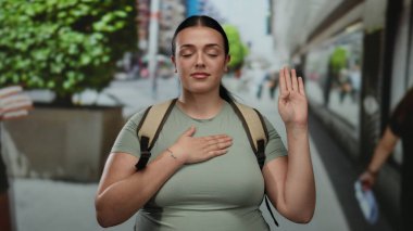 Kendine güveni olan genç bir kadın, arka planda yeşillik olan hareketli bir şehir caddesinde yemin ediyor. Şehir hayatının ortasında kararlılığını gösteriyor..