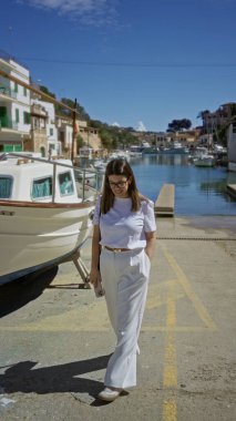 Cala Figür Limanı 'nda gülümseyen bir kadın, Akdeniz boyunca güneşli bir gökyüzünün altına yanaşmış tekneli Mallorca, sakin bir sahil atmosferi yaratıyor..