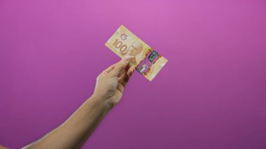 Mor arka planda Kanada doları banknotları tutan adam, finansal kavramları ve döviz takasını canlı ve izole bir şekilde ima ediyor..