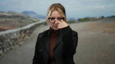 Gözlüklü genç sarışın kadın park ortamında tetikte ve tehditkar hareketler yapıyor. Bu da dikkatli bir varlık ve iddialı bir iletişim olduğunu gösteriyor..