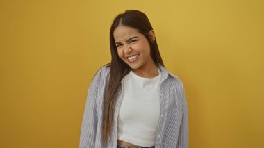 Parlak sarı bir arka plana gülümseyen, esmer saçlarını ve günlük kıyafetlerini gösteren, neşeli bir ifadeyle genç güzelliğini ve çekiciliğini somutlaştıran bir kadın..