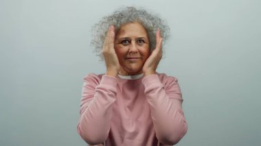 Beyaz tenli arka planda gülümseyen ve yüzünü gösteren gri saçlı yaşlı bir kadın..