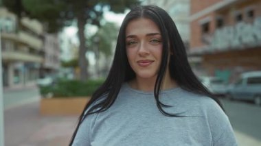 Şehirli bir sokakta güvenle yürüyen kıvrımlı bir kadın, arka planda kentsel binalarla tarzını ve güzelliğini sergiliyor..