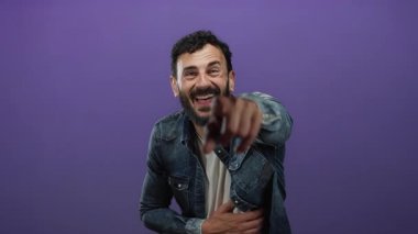 Mutlu İspanyol sakallı adam mor bir arka plan önünde gülüyor kot ceket giyiyor ve neşe saçıyor..