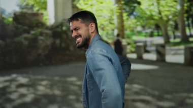 Güneşli bir günde rahat bir ortamda yeşilliklerle çevrili sırt ağrısı çeken bir adam, rahat bir ortamda rahat olmayan, gençlik ve doğa..