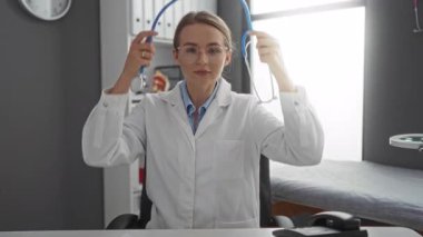 Steteskoplu beyaz önlüklü kadın doktor klinikte tıbbi ekipman ve parlak ışıklandırmayla oturuyor.