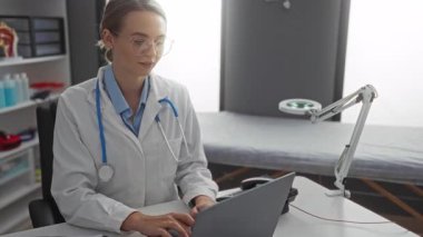 Hastane odasında dizüstü bilgisayarında çalışan kadın doktor yanında tıbbi aletlerle steteskop takıyor, odaklanmış ve profesyonel görünüyor..