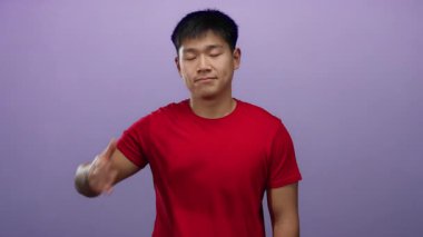 İzole edilmiş mor arka planı olan yüzü kaplayan genç bir adam kırmızı bir gömlek giyiyor, neşeli ve canlı bir ifade sergiliyor..