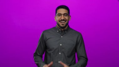 Pembe arka planda gülümseyen yakışıklı, mutlu ve kendinden emin, gözlüklü ve sakallı, koyu renk gömlekli, izole edilmiş bir portrede neşe ve memnuniyet gösteren bir adam..