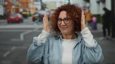 Hareketli bir şehir caddesinde elleri ile çerçeveleme kadın, orta yaş, açık hava düzeni ve canlı kentsel yaşam özünü yakalıyor.